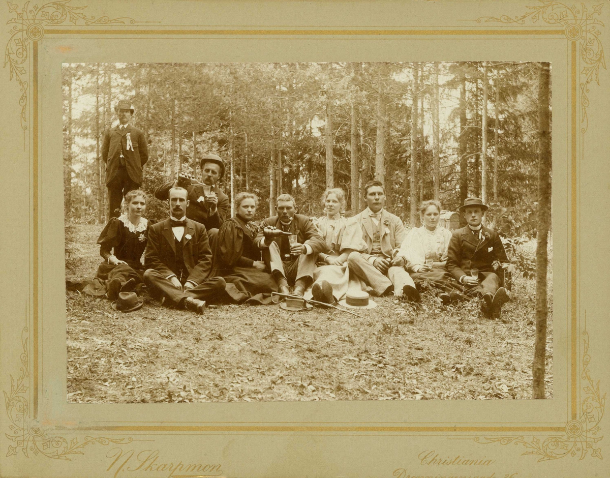 Narve Skarpmoen, Fra en kjøretur til "Tyrigrava", Kolbotn, Oppegård, Akershus 1895 eller 1896. Gruppe sitter oppstilt for fotografering i skogen. Nr.3 og 4 fra høyre er Carl Amundsen og Helga Kristine Jensen.