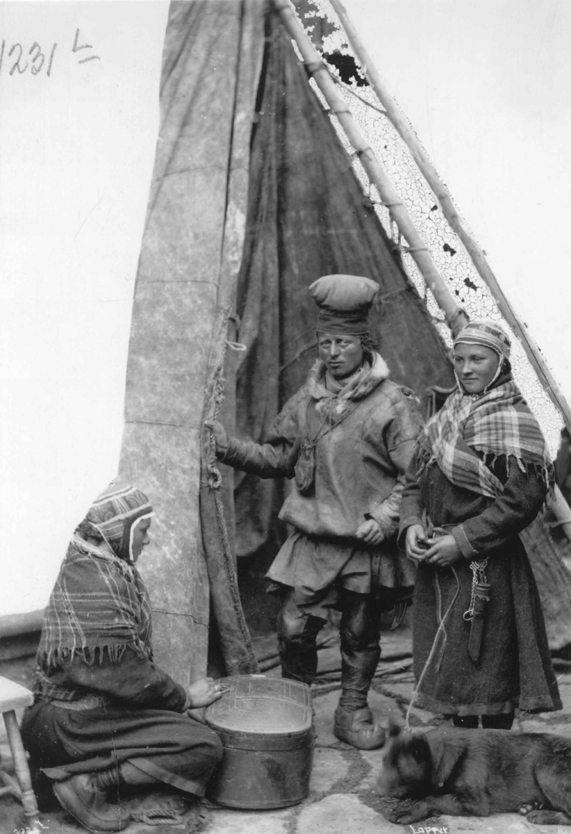 Axel Lindahl, Svenske samer. En mann og to kvinner ved teltåpning. Den ene kvinnen sitter ved en koffert, den andre holder en hund i bånd. Sverige ca. 1885-92.