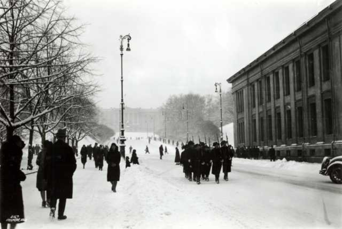 Hermann Christian Neupert, Karl Johan, Oslo 1930. Vinterbilde av mennesker på Karl Johan, sett mot Slottet og med Universitetet på høyre side. Fotgjengere.
