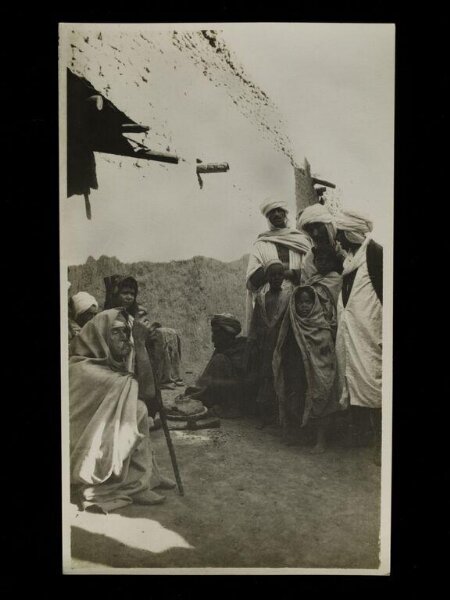Unknown, A group of people, sitting and standing, in a street in Sidi Okba, Algeria.