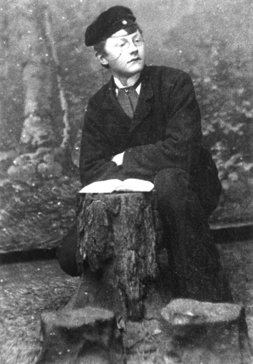 Anna Grostøl, Ung mann sitter ved en stubbe med en bok på, antagelig i et fotostudio. Anna Grostøls familie. Vest-Agder 1941-42.