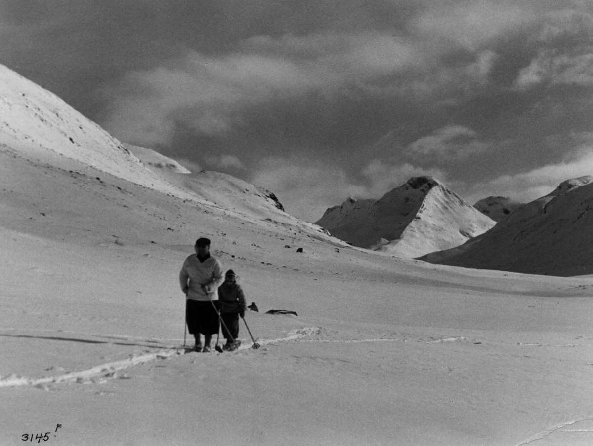 Anders Beer Wilse, Skiløpere i Uladalen i Jotunheimen med snødekte fjell og sol.