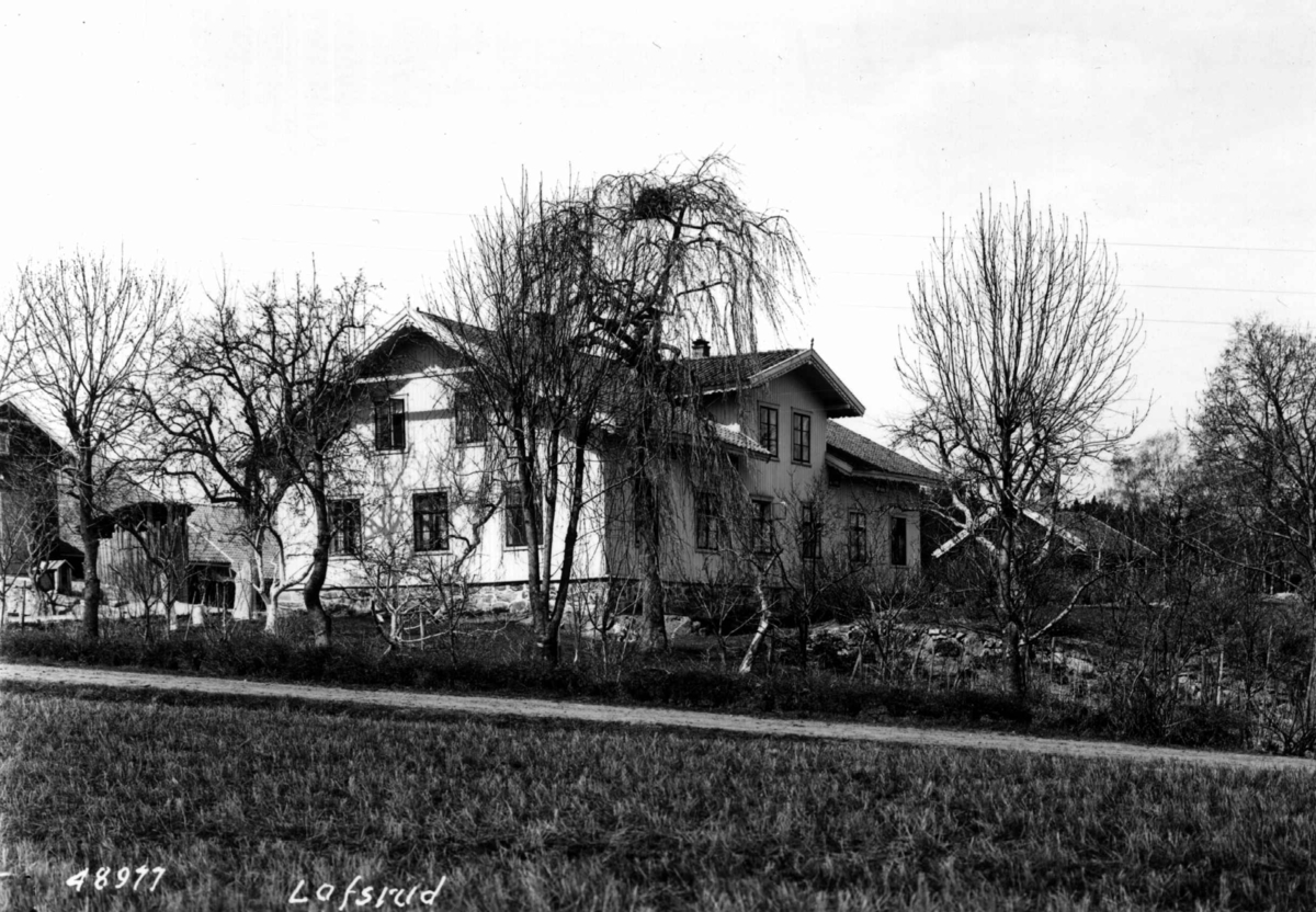 Anders Beer Wilse, Lofsrud gård, Oslo, Østre Aker. Våningshuset, uthus og hagen fotografert fra et jorde.