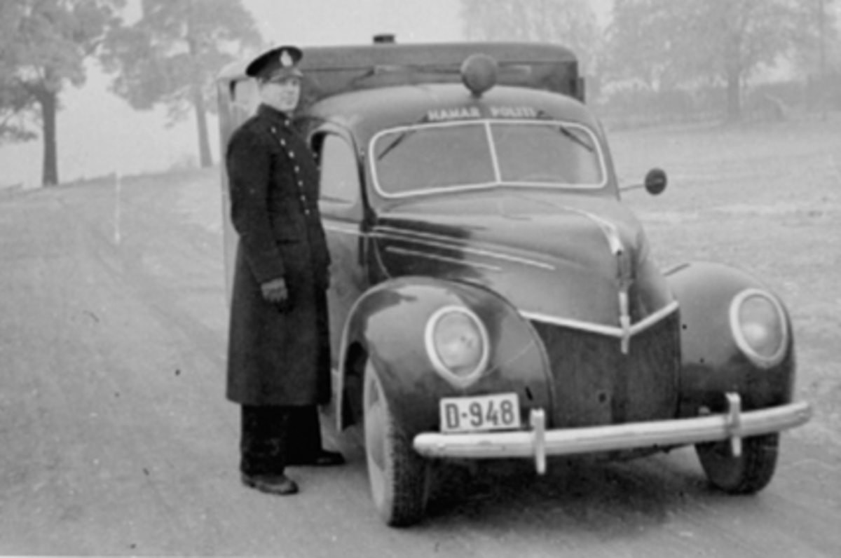 Anno Domkirkeodden, POLITI BIRGER KOLSTAD I POLITIUNIFORM FORAN SVARTEMARJA D-948, POLITIBIL FORD V8 1939 DE LUXE. OPPRINNELIG EN PERSONBIL, KAPPET BAK FØRERSETET OG PÅMONTERT KASSE FOR ARRESTANTER.