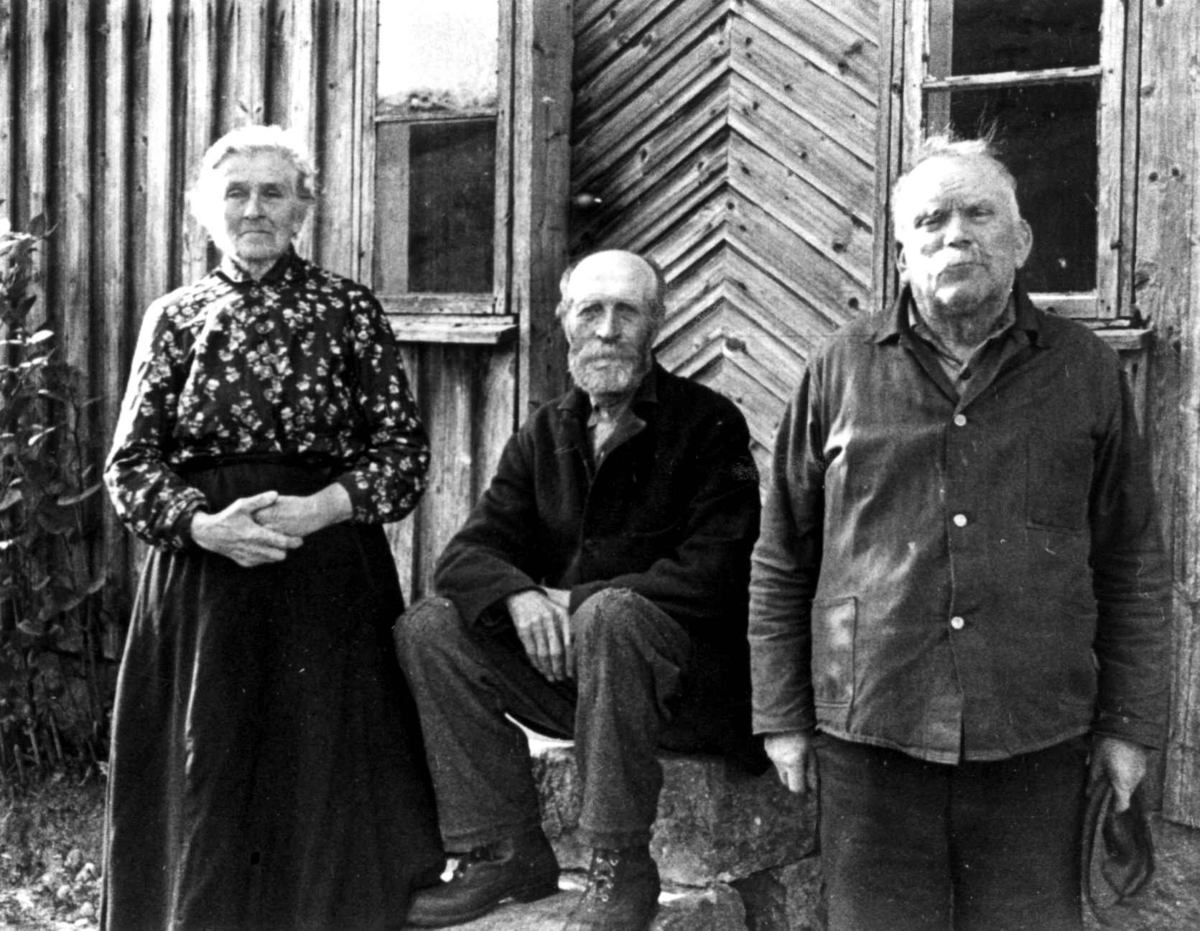 Anna Grostøl, Portrett av Ola H. og Gunvor Røynebo og Per Tobias Kvinlog foran inngangspartiet til et hus. Fjotland, Kvinesdal, 1941.