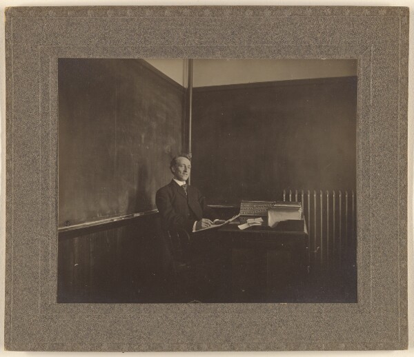 Unknown, [Portrait of a male teacher seated at his classroom desk]
