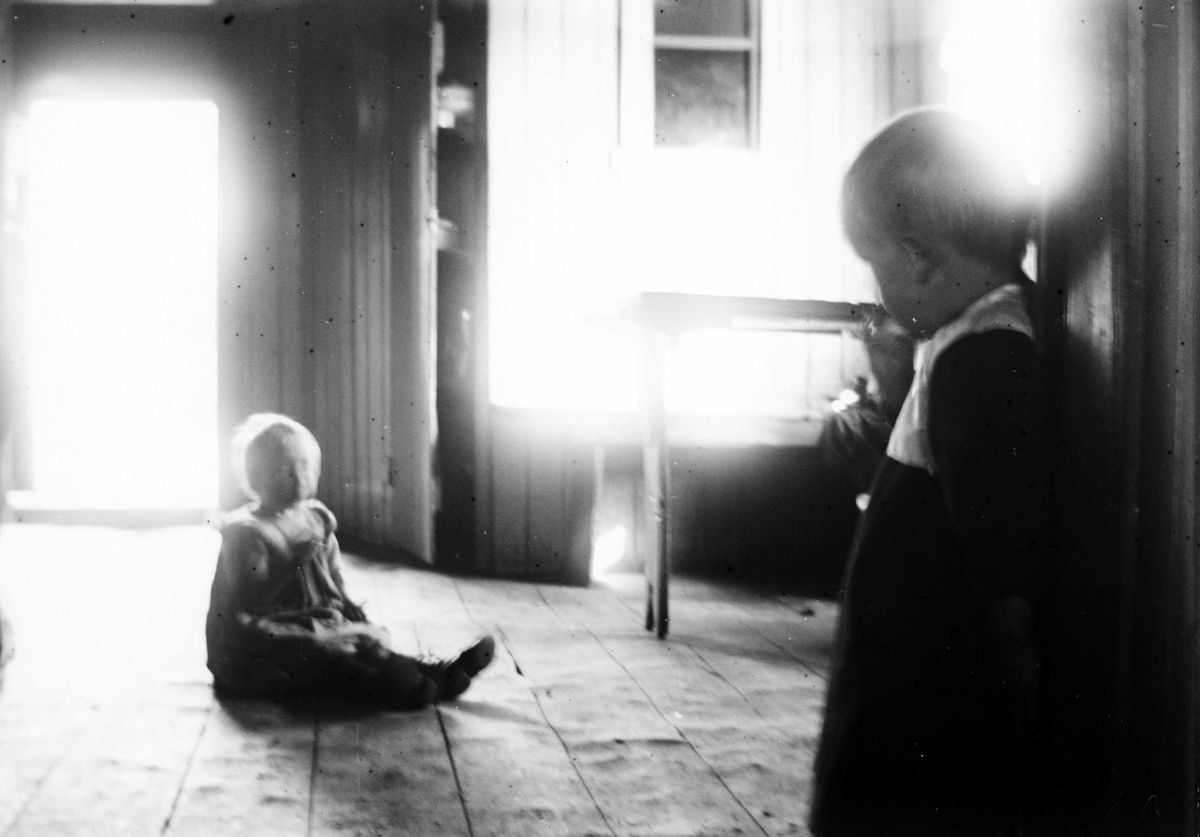 Juliane Fredrikke Langberg, 2 barn i et rom, det ene sittende på kraftig tregulv.Overbelyste partier. Muligens i Hurum. Fra malerinne Juliane Fredrikke Langbergs (1856-1930) samling, tatt ca.1895-1910 med motivkrets slekt og venner samt steder tilknyttet samvær med disse.