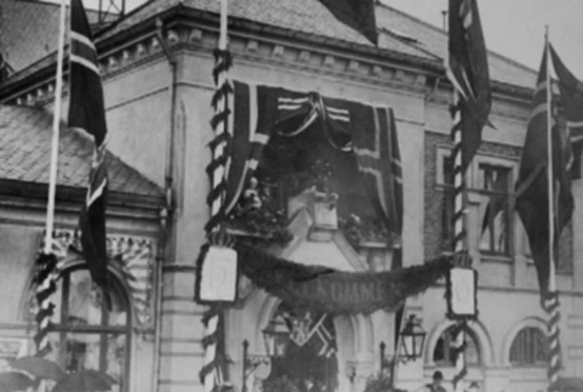 Anno Domkirkeodden, KRONINGSREISE 1906, KONGEFAMILIEN PÅ VERANDA I RESTAURANTBYGGET PÅ HAMAR JERNBANESTASJON, PYNTET MED GIRLANDERE OG FLAGG