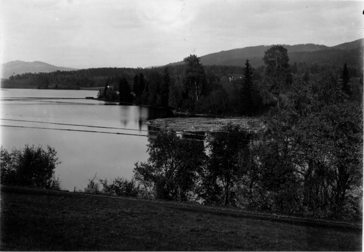 Hermann Christian Neupert, Bogstadvannet, Oslo 1908-10. Oversiktsbilde. Tømmer på vannet. Skog. Bebyggelse i bakgrunnen.