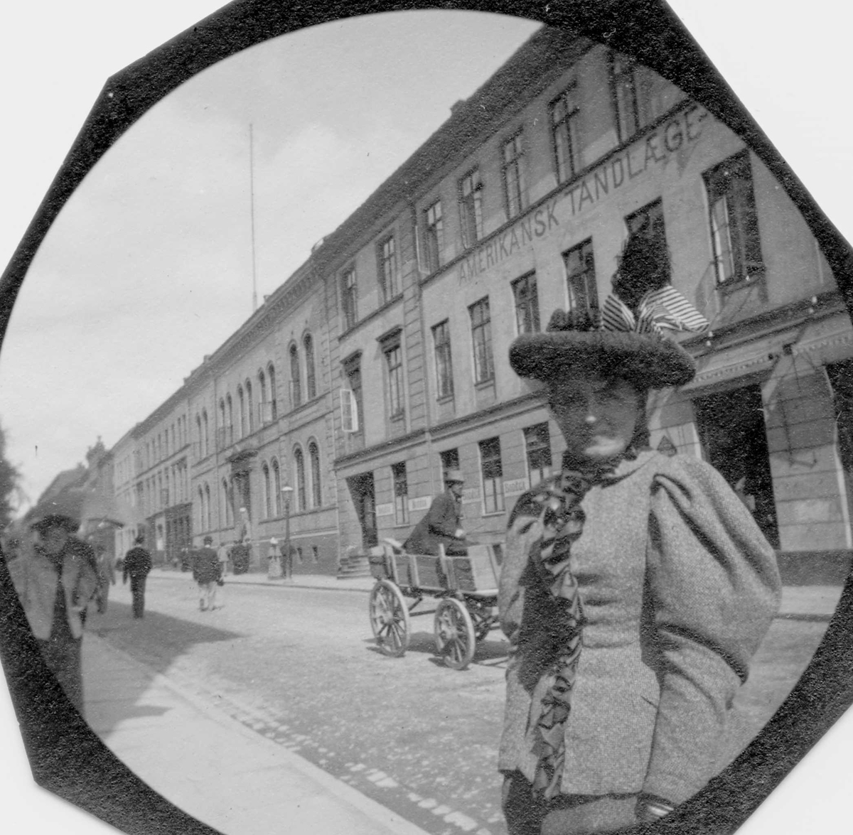 Fredrik Carl Mülertz Størmer, Frk. Magnella Arents (Arentz?)står i bygate, ant. Oslo, med hestekjøretøy i gata. Tannlegeskilt på en husvegg.