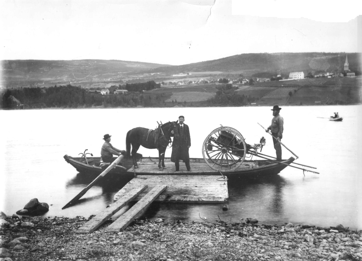 Marthinius Skøien, Fergetrafikk, robåt med to fergemenn frakter hest og kjøretøy over et vann. Personen ved hesten er muligens fotograf Marthinius Skøien selv. Bildet kan være av Lillehammer, tatt fra Vingnes.