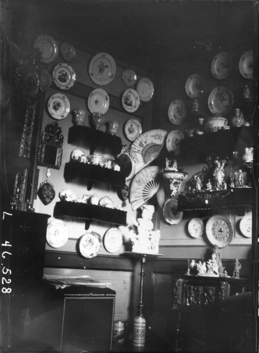 Fredrik Emil Faye, Interiør, Dal gård, Ullensaker. "Porselenskabinettet". Hyller med diverse dekketøy og nips, tallerkner i keramikk hengt opp. Ca. 1898. Fra serie fotografert av kammerherre Fredrik Emil Faye (1844-1903), gårdens eier.