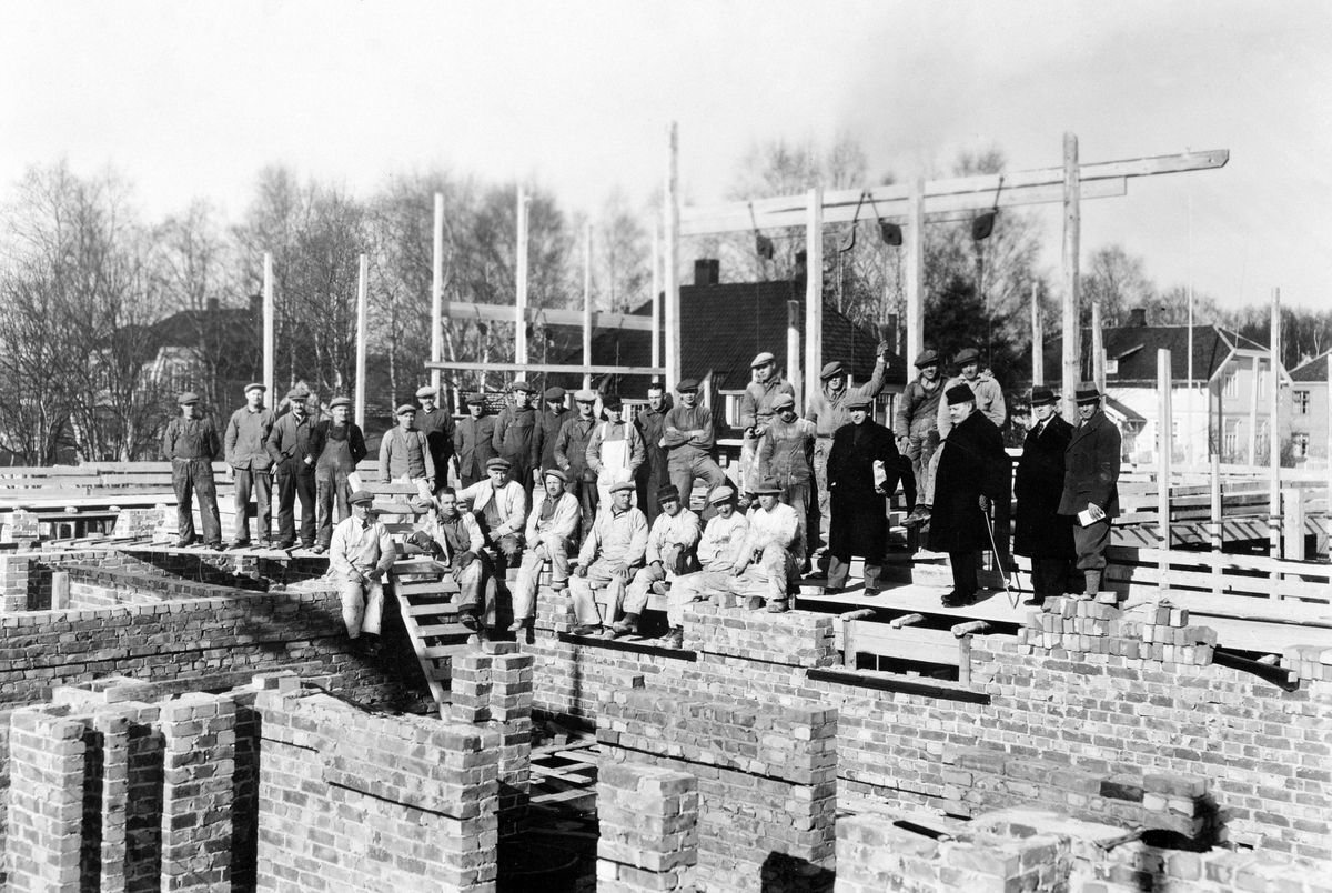 Anno Domkirkeodden, Østregate 102, Hamar. Byggeplass, bygningsarbeidere. Murere i forgrunnen. Murerbasen Gudbrand Kristiansen nr. 3 f.v. De øvrigemurere Kristian Sandlie, Johannes Løvmo, Gustav Jønsson, Hjalmar Johansen, Kristian Fjeldhaug. Murstein, teglstein.