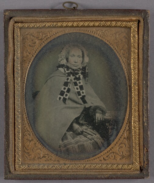 Unknown, [Portrait of a Seated, Middle-aged Woman in Bonnet with Patterned Tie Ribbons and Long Cloak]