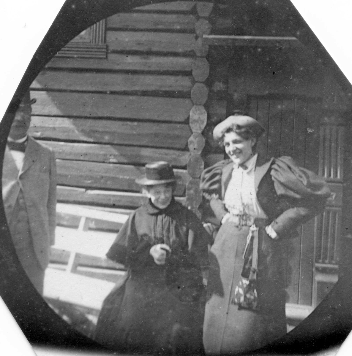 Fredrik Carl Mülertz Størmer, Golå, Sør-Fron, Oppland. En kvinne og en mann står foran tømmerhus. En kvinne sitter på en krakk.