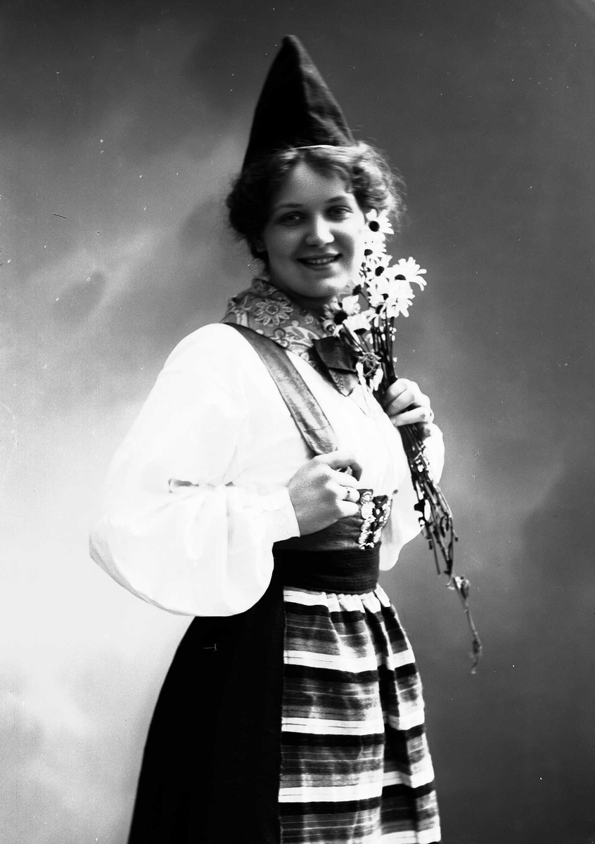 Solveig Lund, Kvinne i drakt og lue, som holder blomsterbukett.