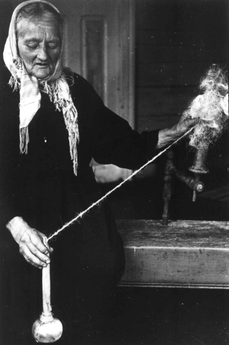 Anna Grostøl, Ragnhild Åvitsland spinner kutagl og grov ull på en liten hjemmelaget håndrokk i tre. Eiken, Hægebostad, Vest-Agder 1941.
