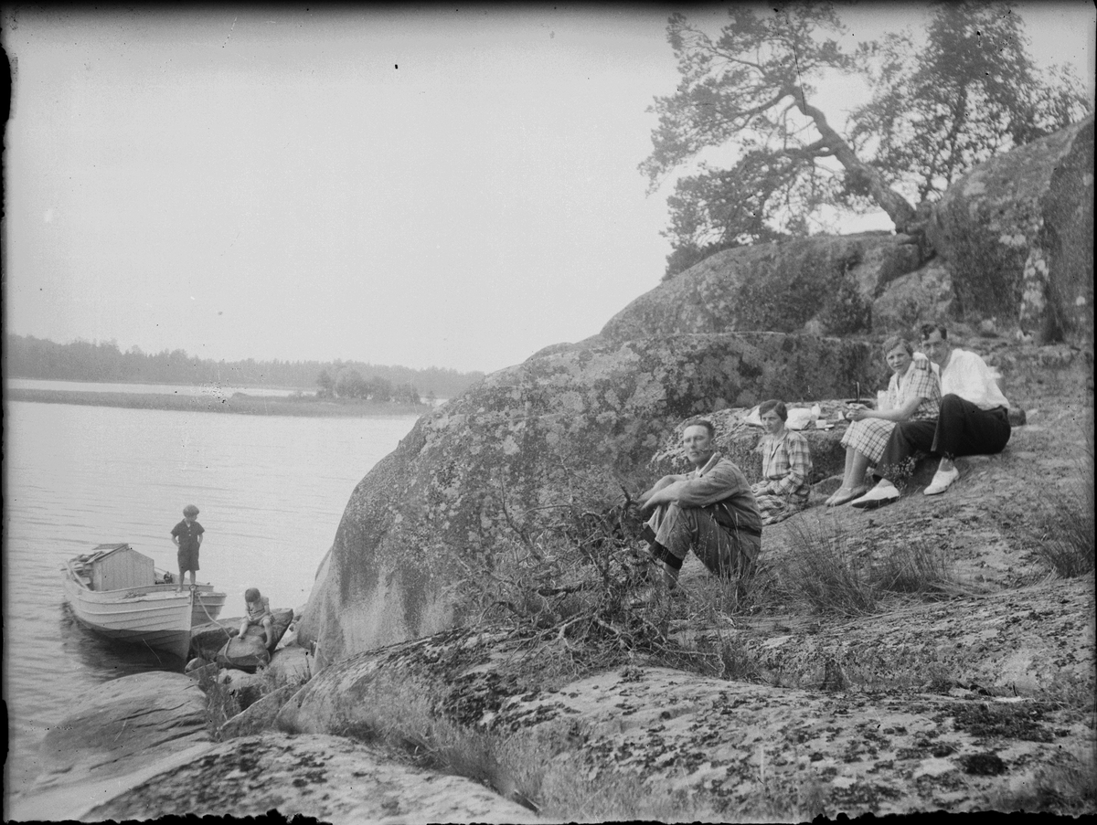 Skötsner-Edhlund, Josef Edhlund sits on the rocks along with a man and two women. Two children are at a boat, Östhammar, Uppland