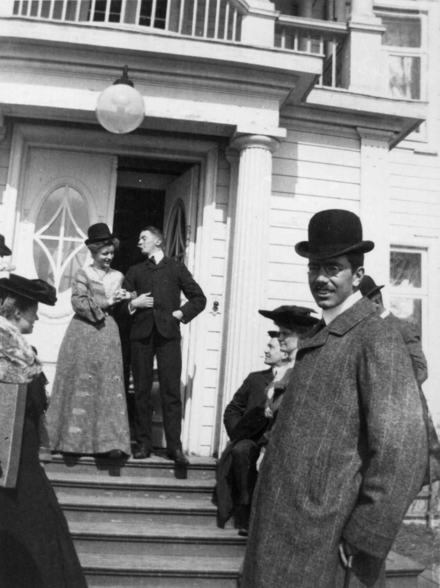 Fredrik Emil Faye, Gruppeportrett, Eidsvold Verk, Eidsvoll. Personer på trapp i inngangsparti med søyler. Muligens tatt 1904. Fra serie antatt fotografert av kammerherre Fredrik Emil Faye (1844-1903), Dal gård, Ullensaker.