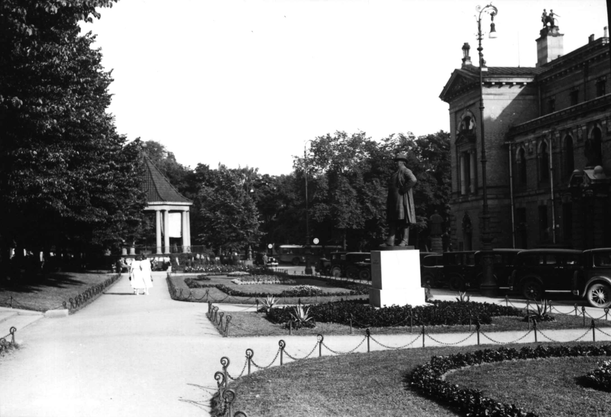 Hermann Christian Neupert, Studenterlunden, Oslo. Nationaltheateret til venstre. Park med statuer og musikkpaviljong. Parkerte biler ses til høyre.