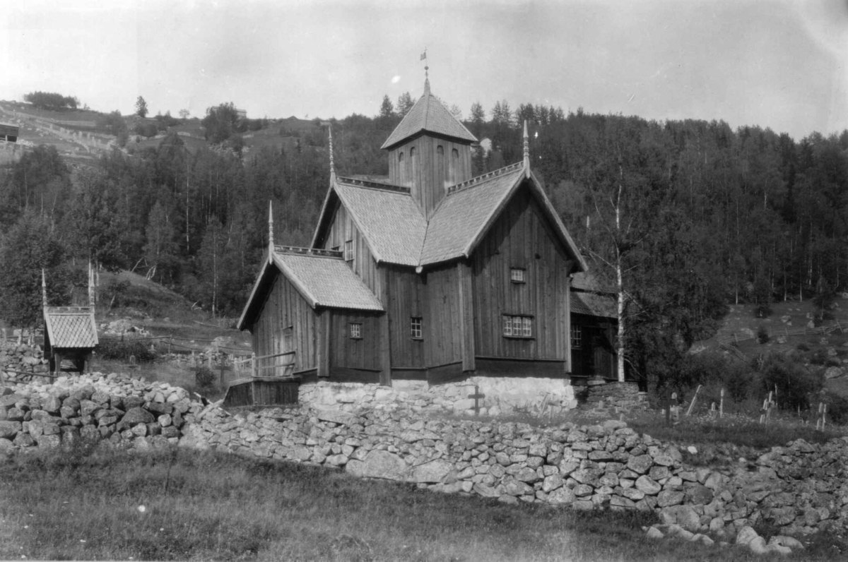 Hermann Christian Neupert, Uvdal kirke, Nore og Uvdal, Buskerud. 1930. Kirkegård. Gravkors. I bakgrunnen landskap med skog og åkrer.