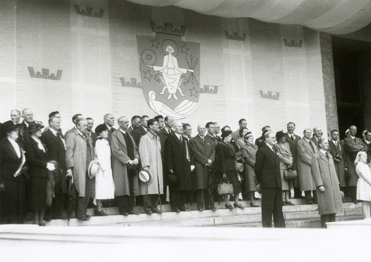 Anders Beer Wilse, Fra Oslo 7. juni 1945. Kongen kommer tilbake. Fra velkomsten utenfor Rådhuset. De prominente gjestene med Oslo Byvåpen i bakgrunnen.