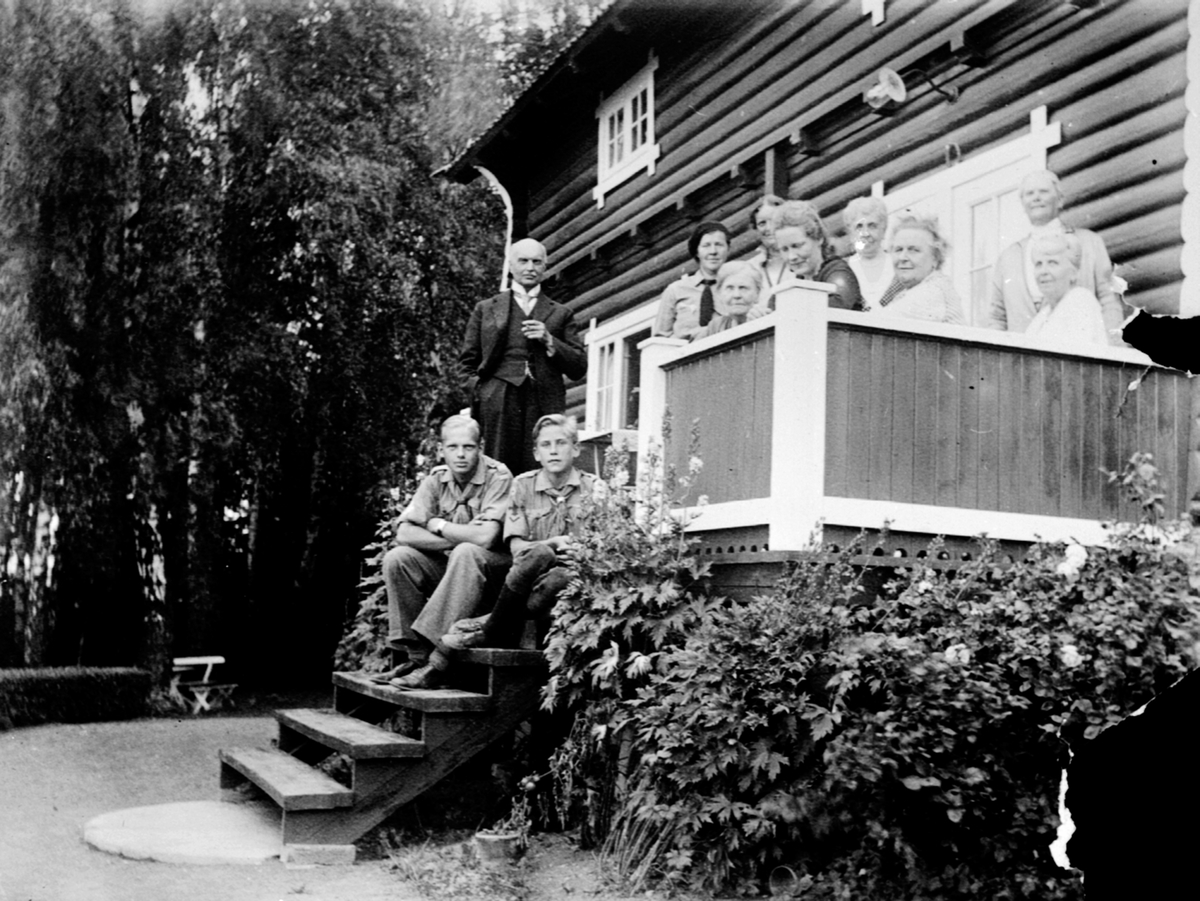 Anno Domkirkeodden, Gruppe personer på verande og i trapp ut mot hagen i Trutterup, Helgøya. Doktor Paul August Hoel i dress. Sittende til venstre i trappa er Wilhelm Olssøn Dybwad.