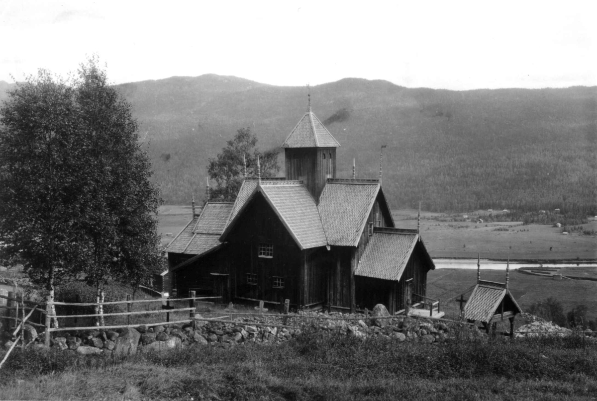 Hermann Christian Neupert, Uvdal kirke, Nore og Uvdal. 1930. Stavkirke. Kirkegård. Gravsteiner. Landskap med jorder, åser og fjell i bakgrunnen,