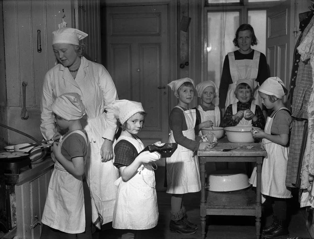 Paul Sandberg, "Småflickor under sakkunnig ledning pröva sin färdighet i matlagning i barnträdgårdens kök" - Etisk-Pedagogiska Institutet, Trädgårdsgatan 12