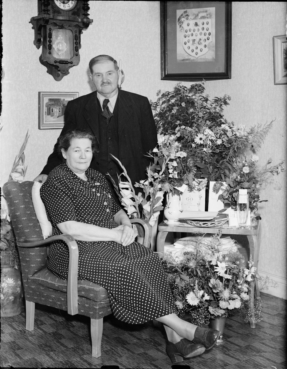 Skötsner-Edhlund, Kvinna och man i hemmiljö omgiven av blommor, Östhammar, Uppland,