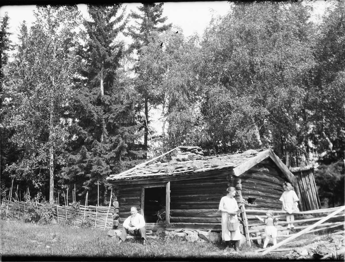 Ragnvald Andersen, Ukjent mann, kvinne og to barn ved ei tømmerhytte i skogen.