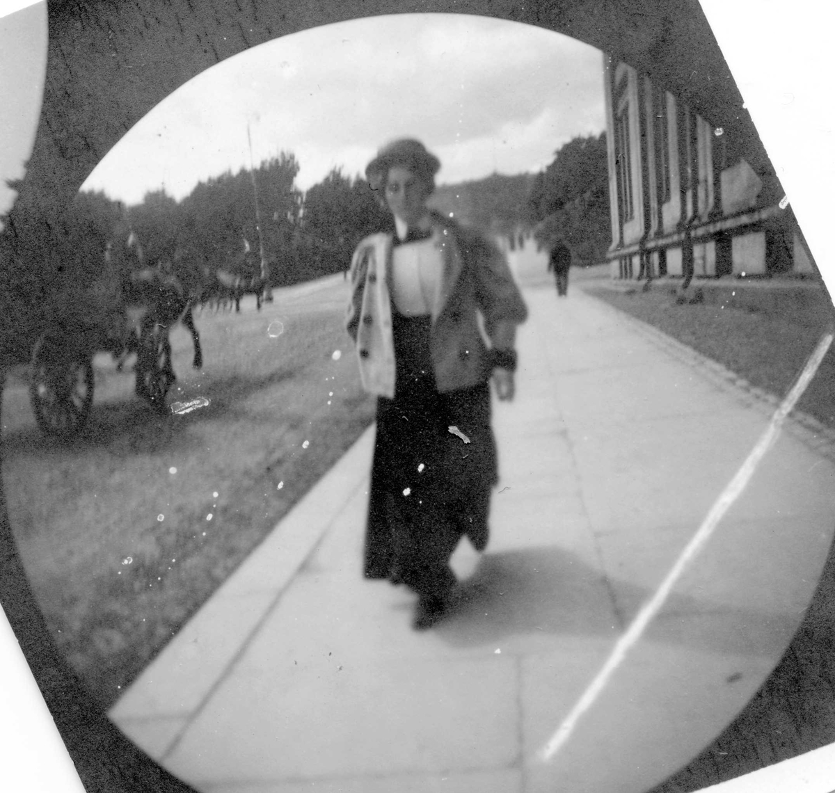 Fredrik Carl Mülertz Størmer, Kvinne spaserer langs Karl Johans gate, Oslo, ved Universitetet. Hestekjøretøy i gata og Slottet skimtes..