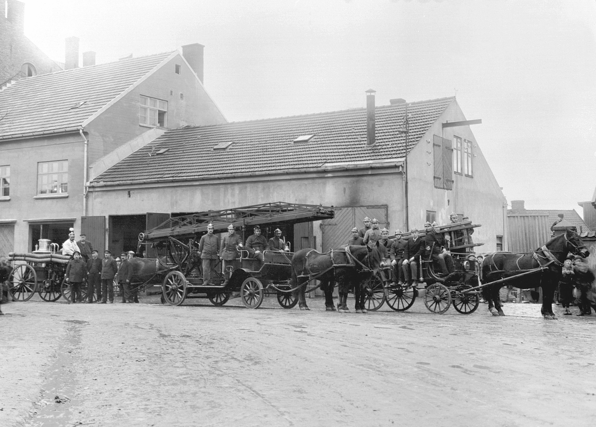 Anno Domkirkeodden, Stor gruppe brannmenn, brannmanskap, utenfor Hamar brannstasjon. Utrykningsmateriell med bl. a. vogn med dampsprøyte til venstre og stigevogn i midten. Dette bildet ble tatt i forbindelse med utskifting fra hestetrukne vogner til biler. Se 0401-02407.