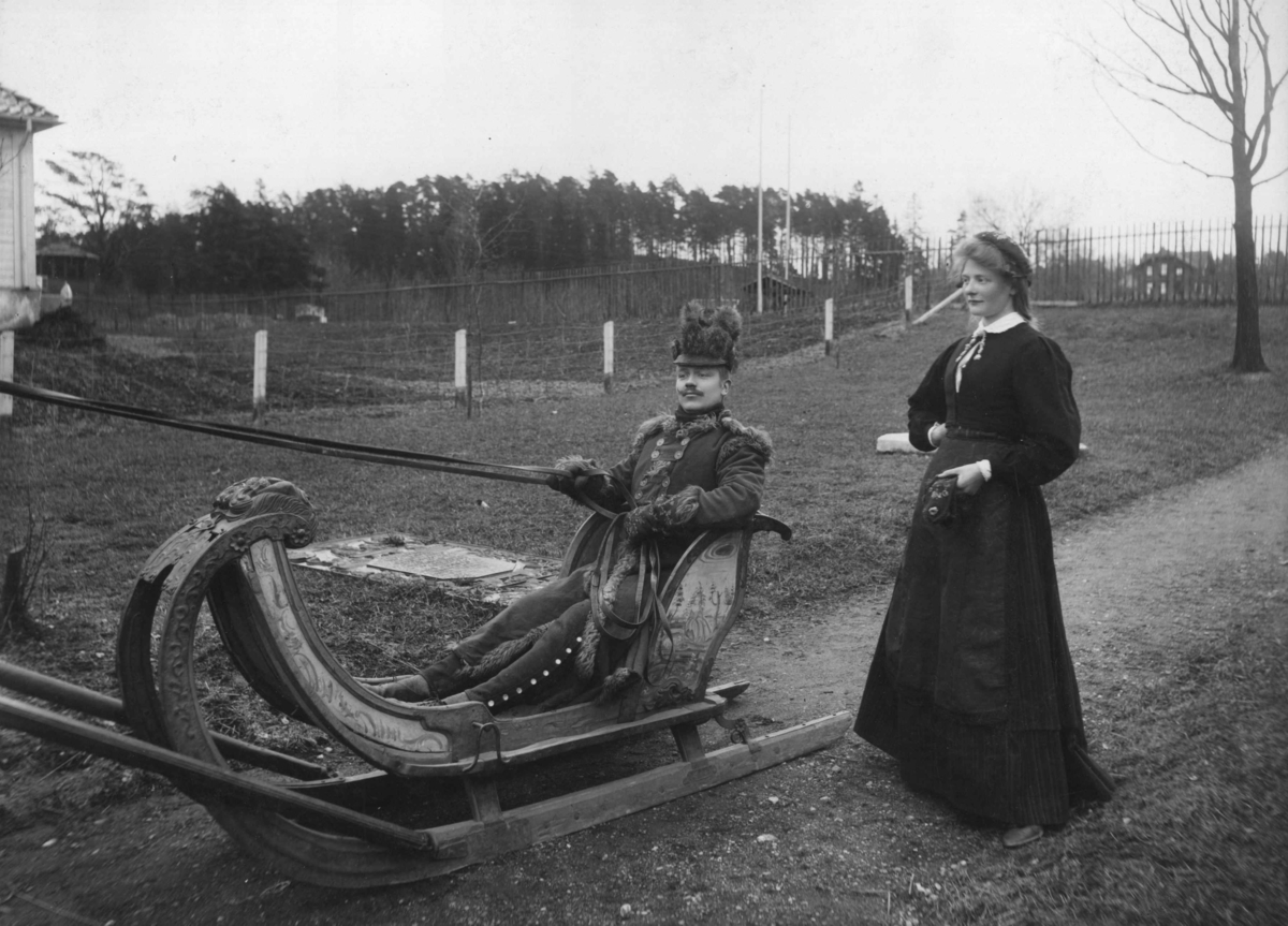 Narve Skarpmoen, Tilstelning, i 1902, på Norsk Folkemuseum. Kvinne og mann i drakter, mannen sittende i en spiss-slede.