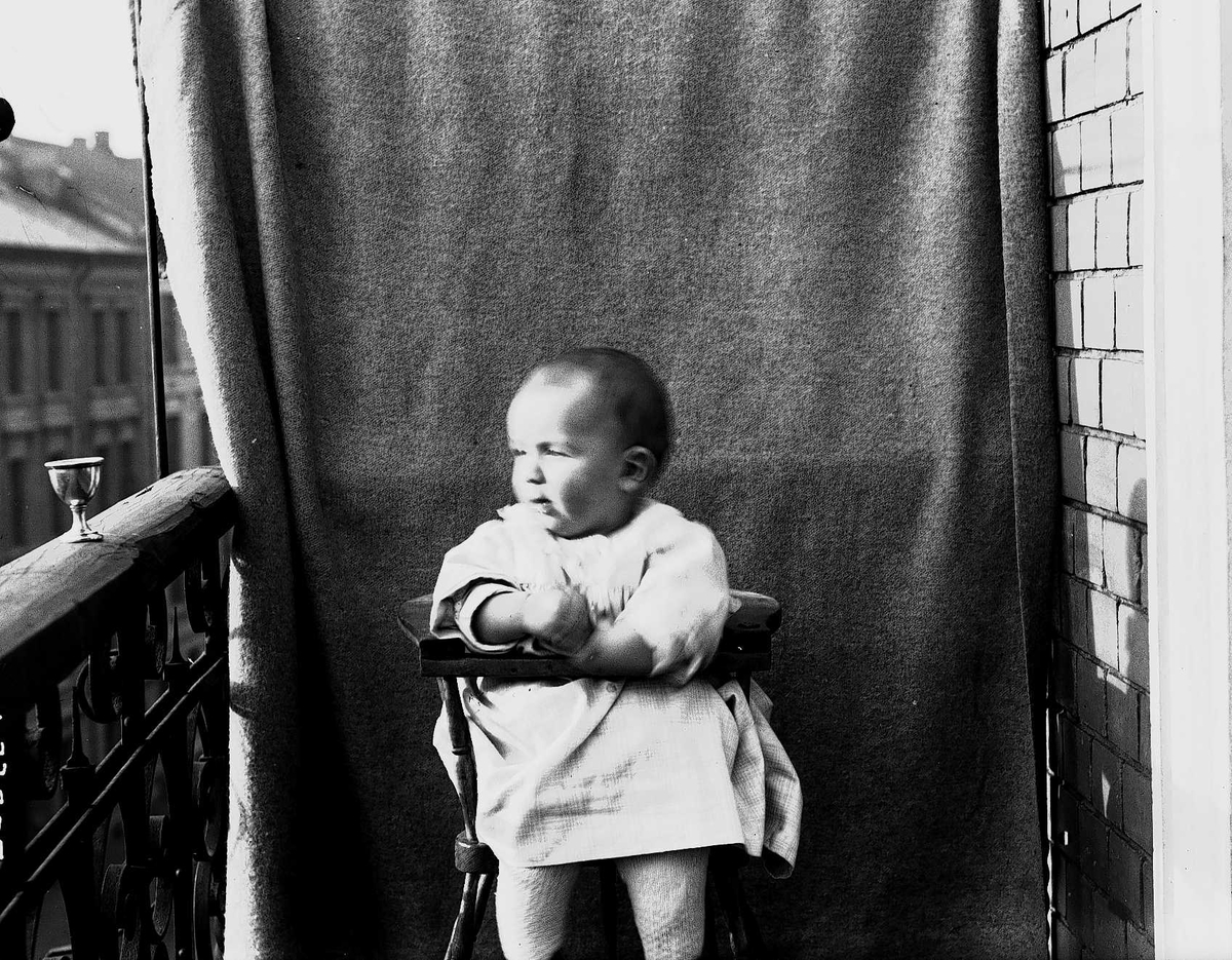 Axel Quinsgaard Wiborg, Lillebror Axel Q. Wiborg i barnestol fotografert på balkong, ant. Meltzers gate 9, Oslo, oktober 1899, mot opphengt bakteppe.