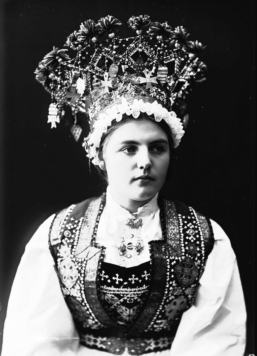 Solveig Lund, Studiofotografi av kvinne med brudedrakt og brudekrone fra Voss i Hordaland. Sittende. Bryst/hofteutsnitt. Frontalt vendt. Ser ut mot høyre.