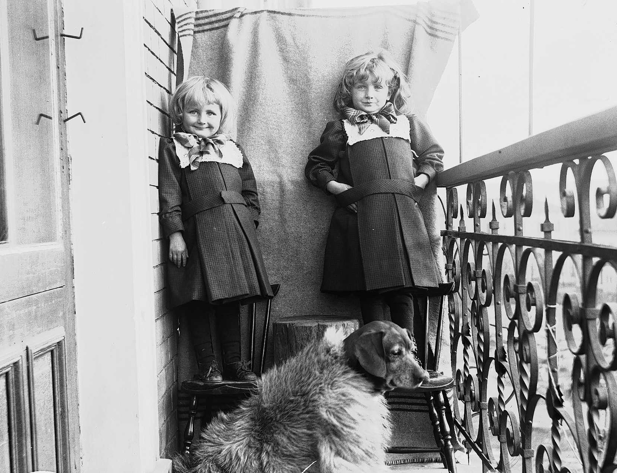 Axel Quinsgaard Wiborg, Karen og Gudrun Q. Wiborg med hund fotografert på balkong, antatt Meltzers gate 9, Oslo, 1899, mot opphengt bakteppe.