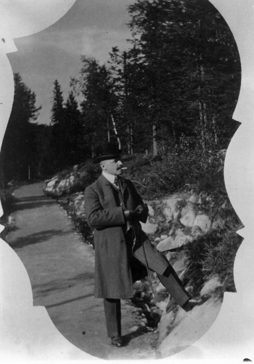Hermann Christian Neupert, Drakt. Oslo 1908-10. Skog. Vei. I forgrunnen mann i frakk og med hatt.