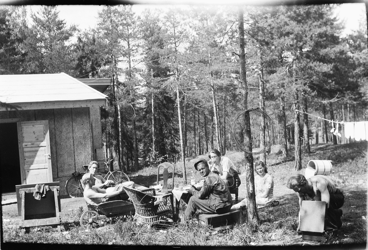 Håkon Prestkværn, Fem menn og en kvinne sitter rundt et bord foran et hus.