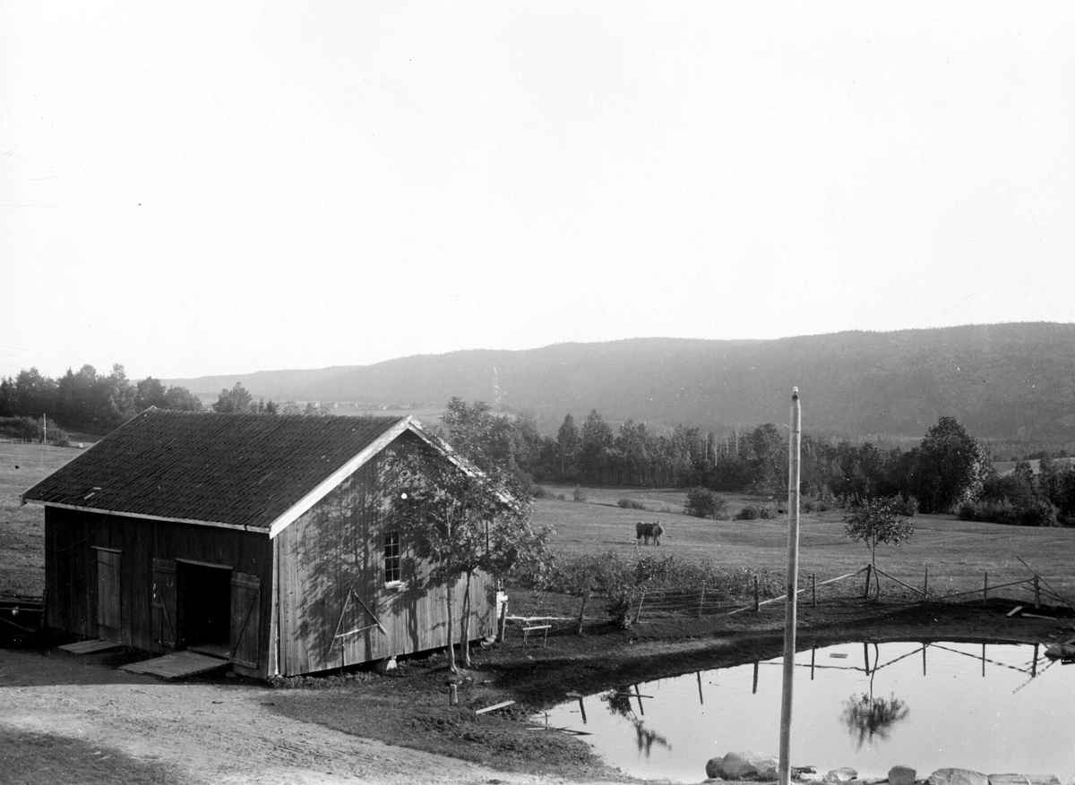 Juliane Fredrikke Langberg, Hurum prestegård, gårdstun med vanningsplass og inngjerdet beiteområde i bakgrunnen. Driftsbygning foran t.v. Fra malerinne Juliane Fredrikke Langbergs (1856-1930) samling, tatt ca.1895-1910 med motivkrets slekt og venner samt steder tilknyttet samvær med disse.