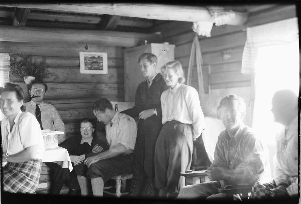 Håkon Prestkværn, Interiør, hytte. Gruppe kvinner og menn. Fra venstre Ingeborg Haugen, Lars R. Haugen, ukjent, ukjent, Arne Vea, Agnes Vea, Mikael Eriksen, ukjent