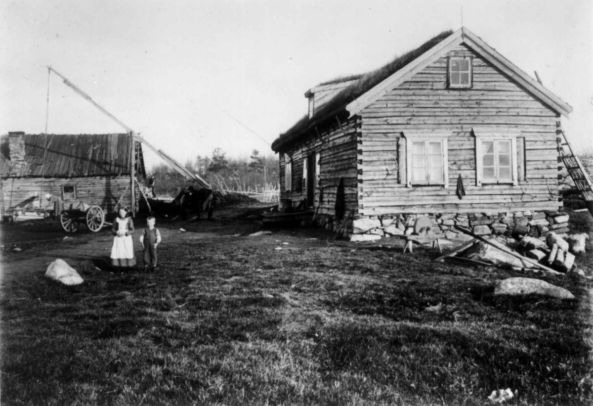 Ellisif Rannveig Wessel, Gårdstun, Svanvik, Sør-Varanger, Finnmark, ukjent år. Gårdsbebyggelse med bolighus og uthus, tun med vippebrønn, kjerre, slipestein og to barn i forgrunnen. Dyrlege Hans Kirkgaards hus.