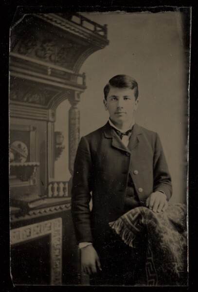Unknown, [Unidentified man standing, with one hand on a chair back]