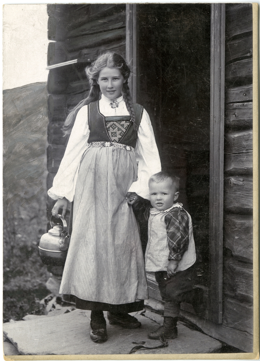 Solveig Lund, Fotografi av jente med drakt og gutt foran dør til bu. Hardanger.
