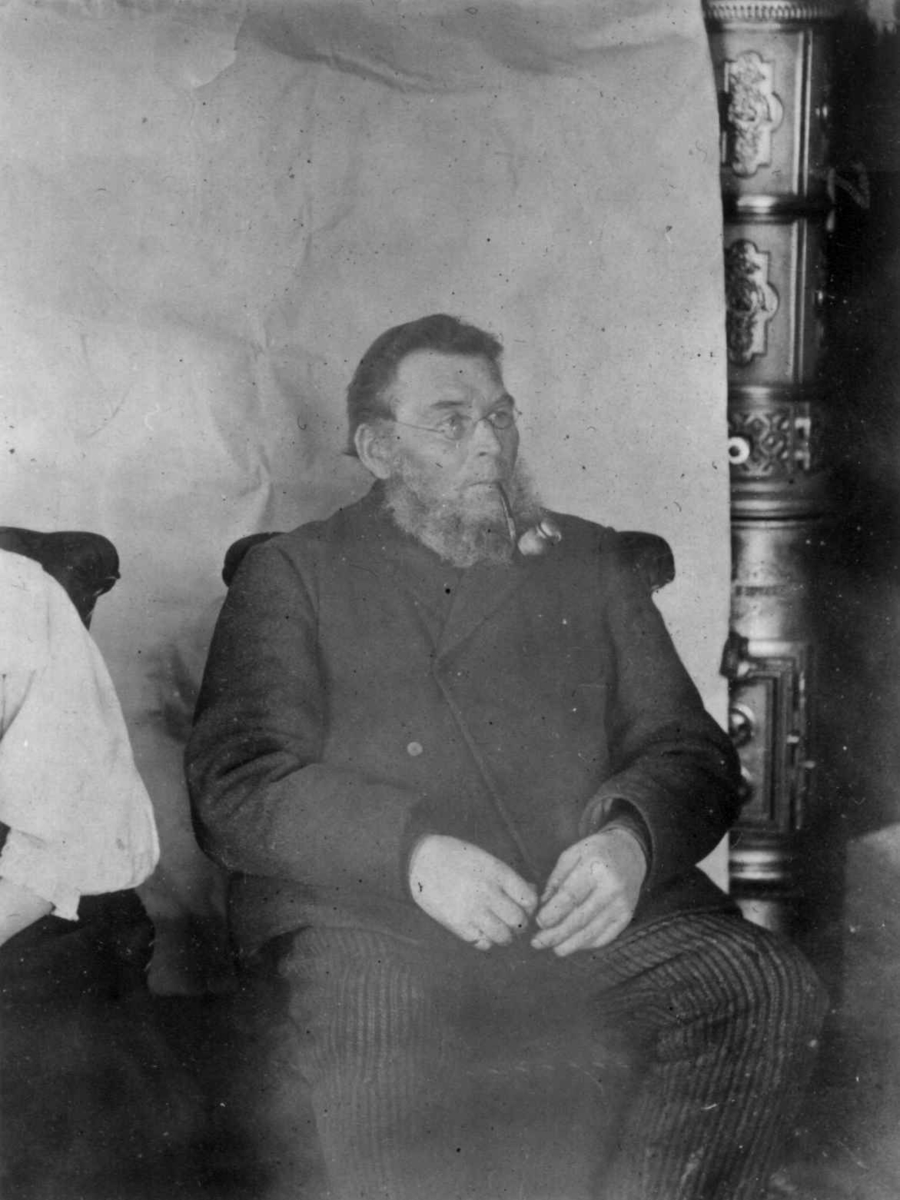 Ellisif Rannveig Wessel, Portrett av Johan Grøn (1842-1920), kven fra Bugøynes, Sør-Varanger, Finnmark. Ukjent år. Han er fotografert i et interiør i doktorgården Solheim, Kirkenes, Sør-Varanger, Finnmark - ekteparet Wessels hjem. Provisorisk bakteppe hengt opp.