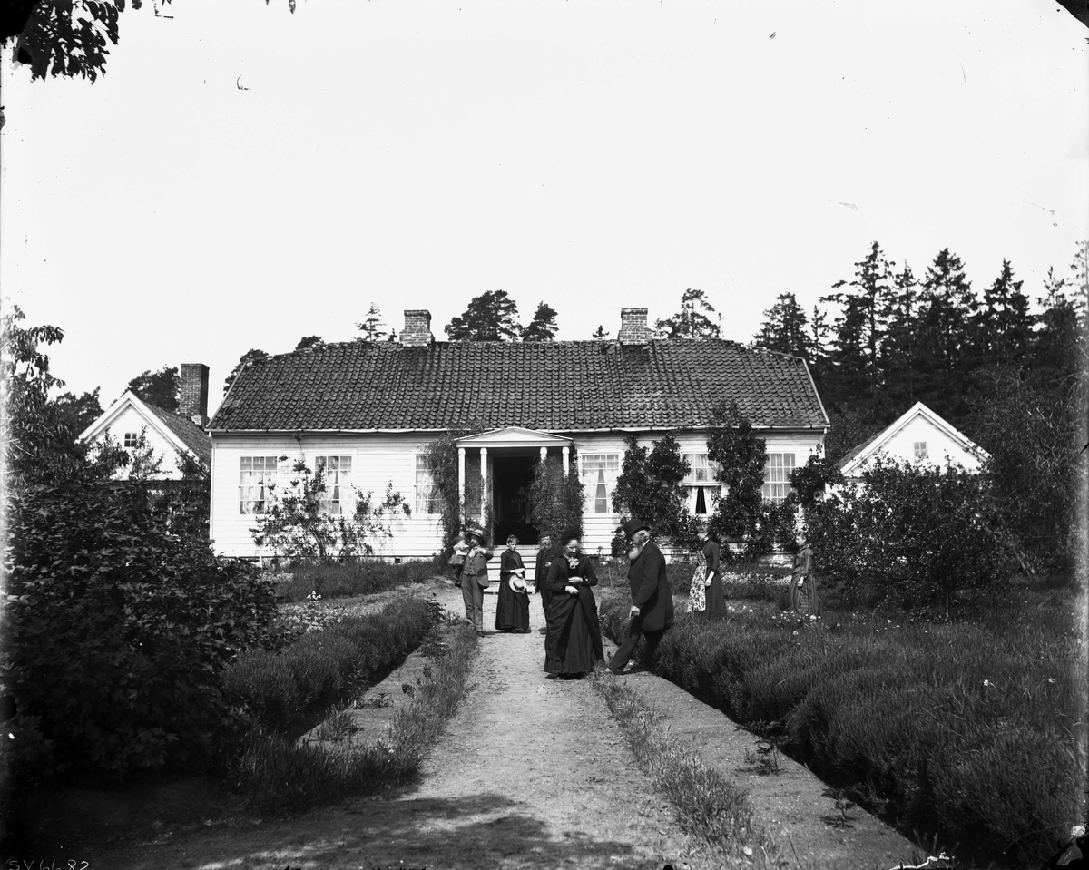 Marthinius Skøien, Gruppeportrett, persongruppe foran våningshus, ukjent sted. Huset har søyleparti og hage omkring.