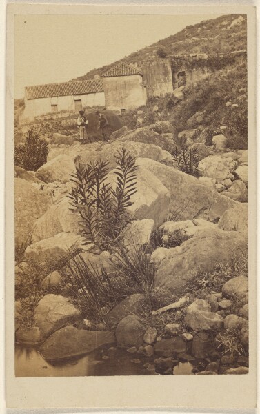 Unknown, [Unidentified rocky landscape with two people and houses in the background]