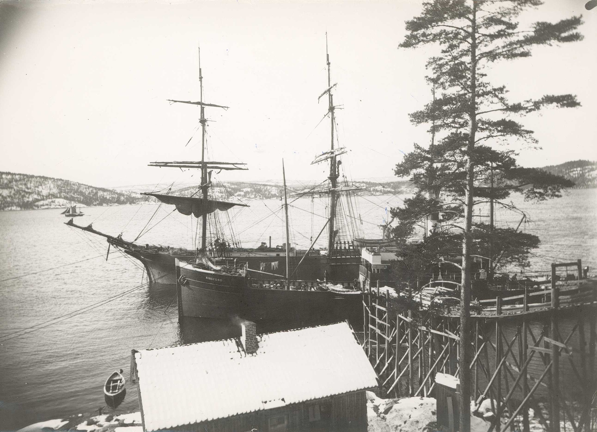 Axel Quinsgaard Wiborg, Islasting ved Sønderstøen i Frogn nær Nesodden i Akershus i 1907. Seil- og dampskip, D/S "Ringfond", ved land med reisverk i tre med renne for lasting av isblokker fra land. Fra serie tatt av iseksportør Axel Quinsgaard Wiborg (d. 1944).