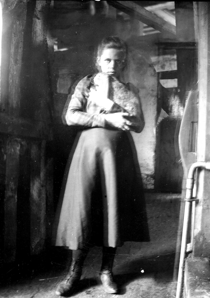 Juliane Fredrikke Langberg, Portrett av jente, Emily Holm, fotografens niese, stående i uthus el.lign. i bluse, halvlangt skjørt og snørestøvler. Dobbelteksponert. Muligens tatt i Hurum eller Rakkestad. Fra malerinne Juliane Fredrikke Langbergs (1856-1930) samling, tatt ca.1895-1910 med motivkrets slekt og venner samt steder …