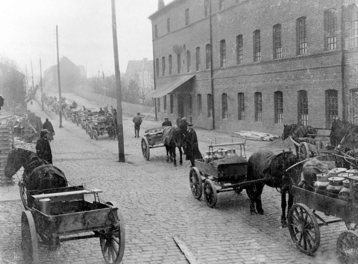 Anno Domkirkeodden, A/S De Norske Melkefabrikker, Melkefabrikken i Storhamargata 52, Hamar. Kokeriet, melkekjørere i kø for levering. Hester med vogner, kusker. Varetransport, hestekjøretøy.